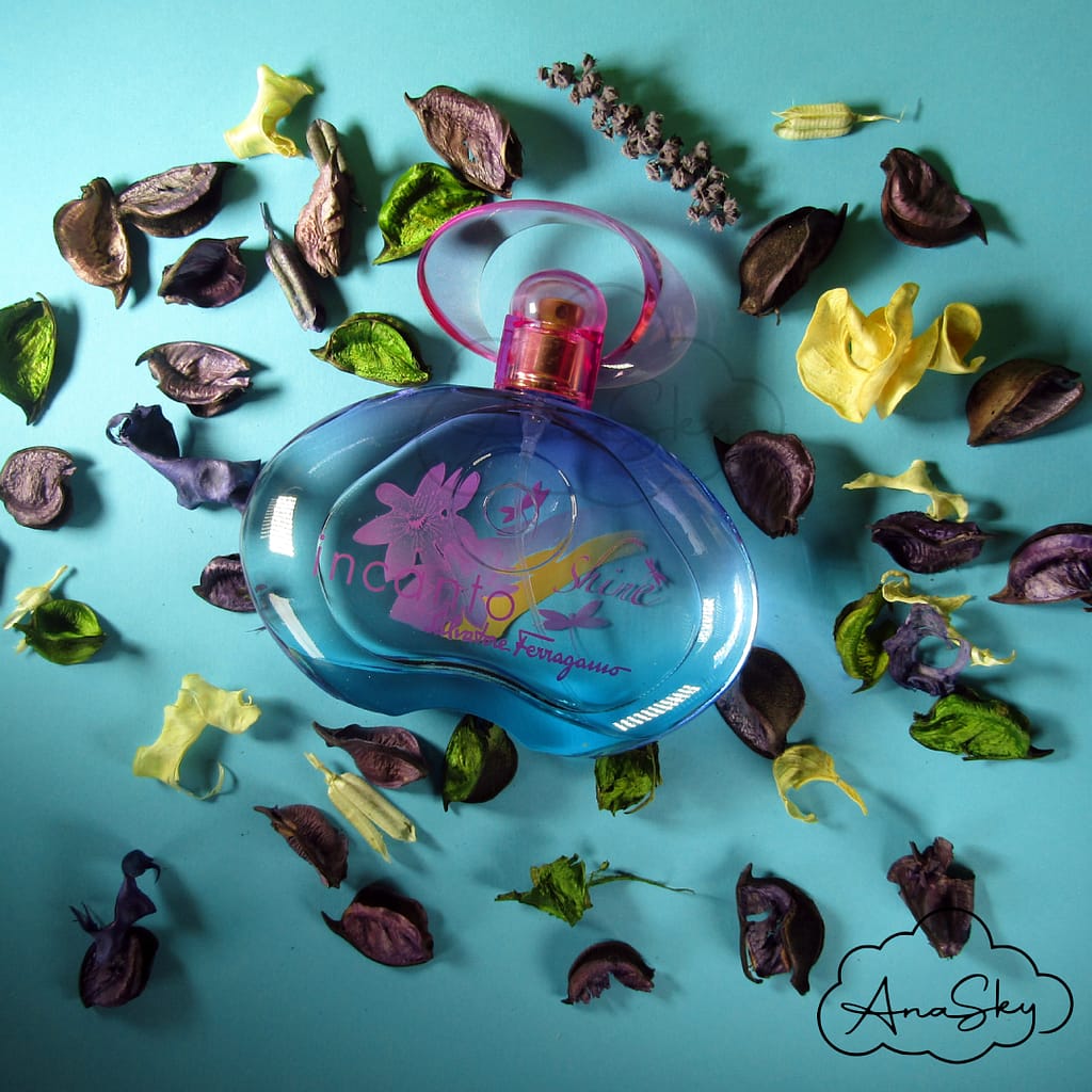 flakon perfum incanto leżący wśród płatków kwiatów na niebieskim tle